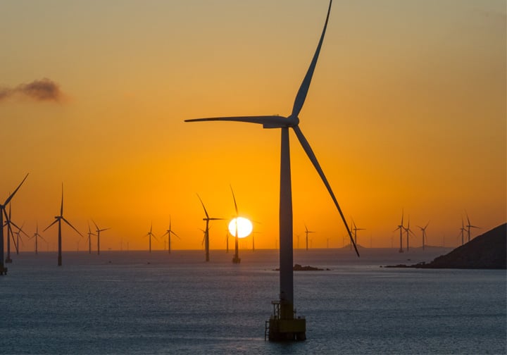 An offshore wind farm in front of an orange sky. 