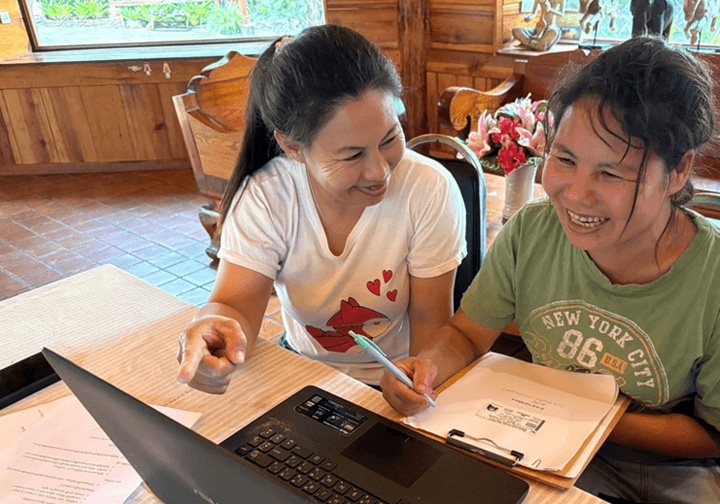 Two women sit at a laptop. 