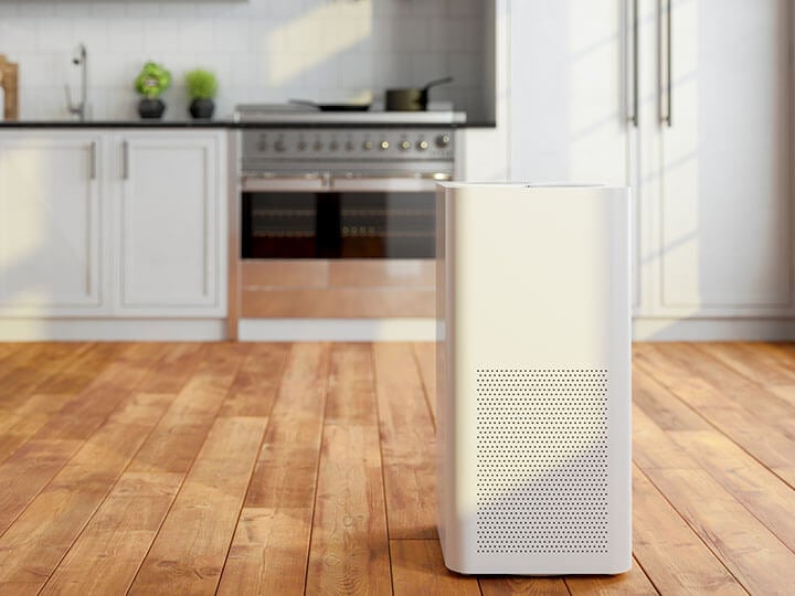 White room air purifier in a kitchen with white cabinets and wooden hardwood floors