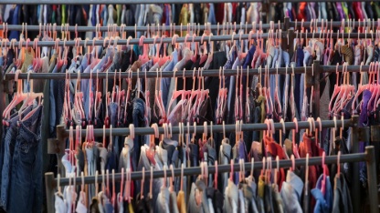 Huge selection of different used clothes for men, women and children on the rack in a second hand shop or thrift store. Concept of waste problem in fashion industry.