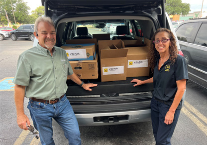 Two Intertek employees stand in front of a car boot full of donated supplies. 