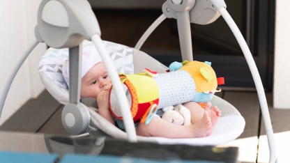 Close up of little 6 months old sweet baby girl in electric swing or cradle outdoors on sunny summer day. Infant background