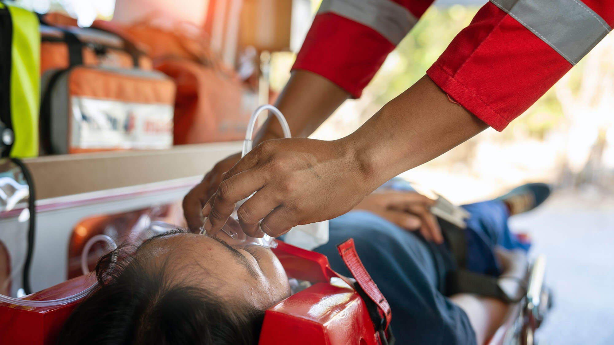 Emergency medical service male nurse rescuer helping a male patient lie on a board performing chest compressions and connecting to a ventilator in an ambulance