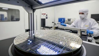 Technician in lab suit working with silicon wafer in a cleanroom with bright lighting. 