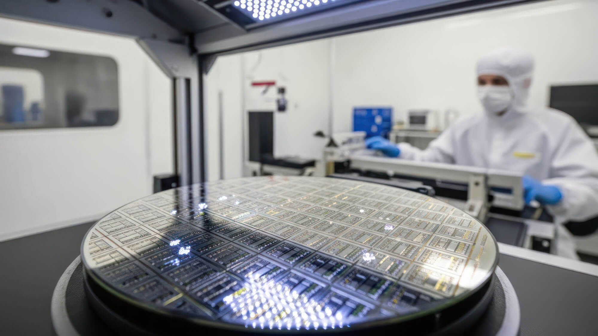 Technician in lab suit working with silicon wafer in a cleanroom with bright lighting. 