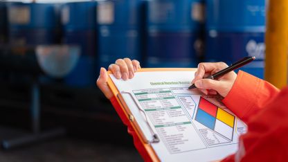Chemical worker completing a Chemical Hazardous Materials identification form on a clipboard in an industrial facility.