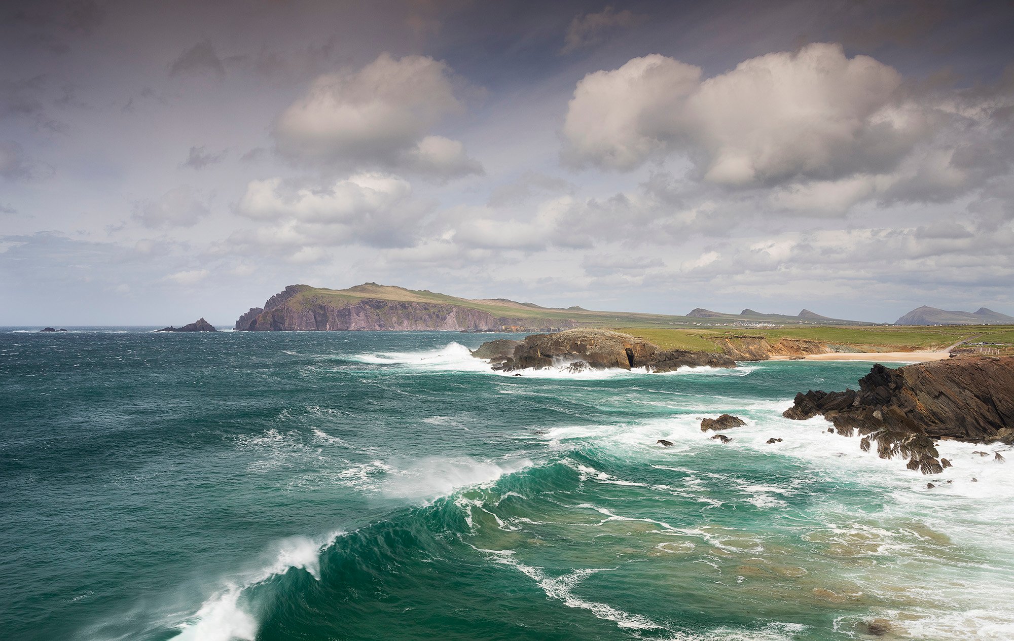turquoise ocean water with cliffs in the background and waves crashing ashore 