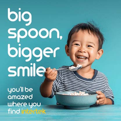 Young boy smiling while holding a spoon over a bowl of food
